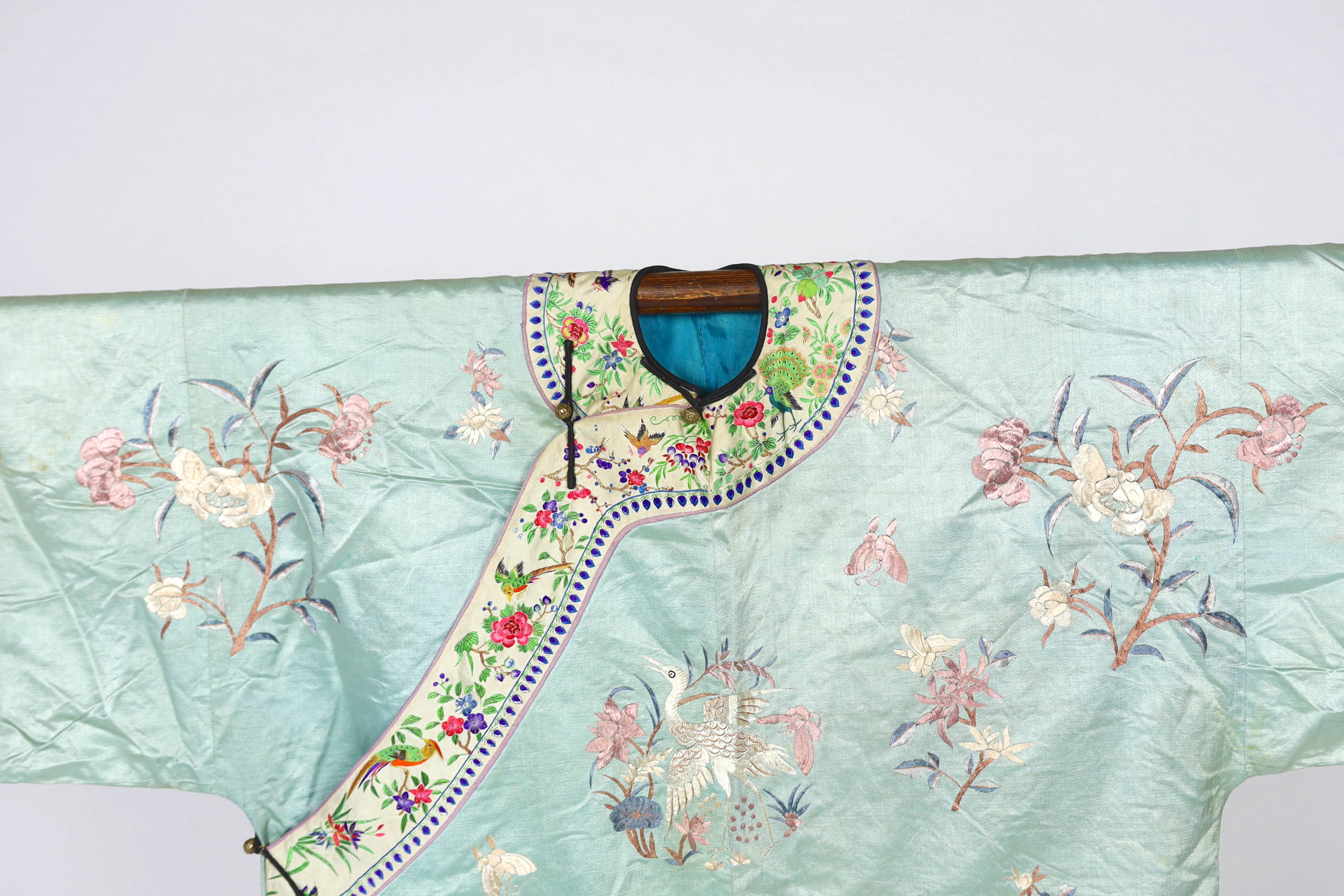 An early 20th century Chinese silk embroidered turquoise robe, embroidered in pastel silk with butterflies and flowers all over, polychrome embroidered braiding edged with lilac and bright pink sleeve bands embroidered w